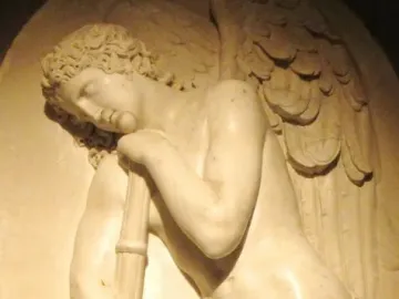 Marble bas-relief of a winged nude male figure leaning on an inverted torch with a rose garland.