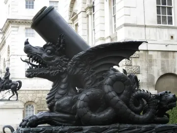 The Cádiz Memorial shows a large mortar mounted on a dark dragon-like sculpture, with a white building and equestrian statue in the background.