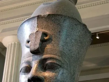 Colossal granite head of Amenhotep III displayed on a white pedestal in a museum