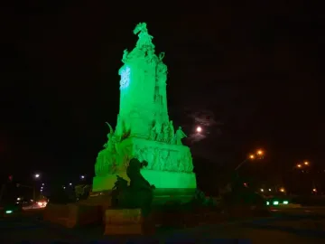 Monument to the Carta Magna and Four Regions of Argentina lit in green at night, with a full moon beside it.