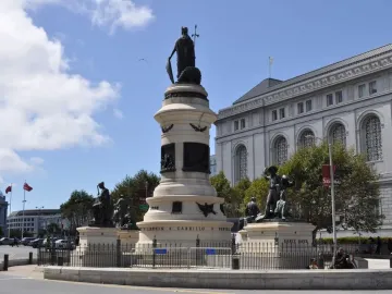 The rear of the Pioneer Monument, a multi-tiered stone monument topped by a robed figure holding a shield and spear, with bronze statues around the base.