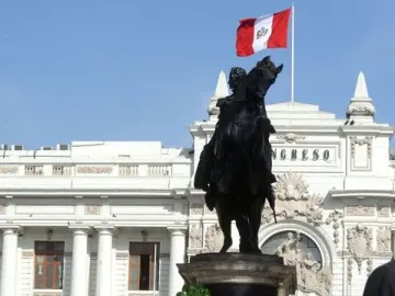 Equestrian statue of Simón Bolívar in front of a grand white building, with a Peruvian flag above and a floral wreath at the base.