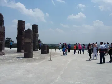 Tall stone Atlantean Figures at Tula standing on a wide plaza with tourists and a bright blue sky overhead.
