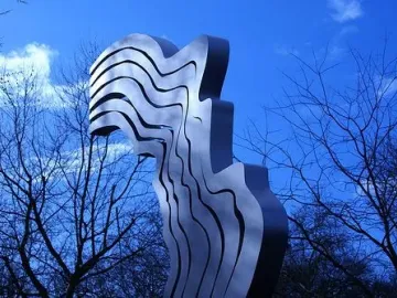 De Schreeuw sculpture against a deep blue sky with leafless tree branches