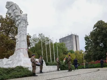 The Monument to the Battle of Monte Cassino stands in a park as soldiers gather around its base during a ceremony.
