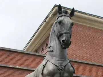 Monument to General Carlos M. de Alvear featuring a dark bronze horse statue with one front leg raised in front of a red brick building.