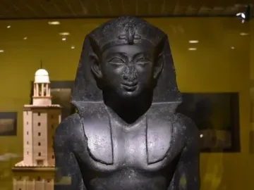 Upper portion of a Ptolemaic King statue with a headdress, damaged nose, and missing arms.