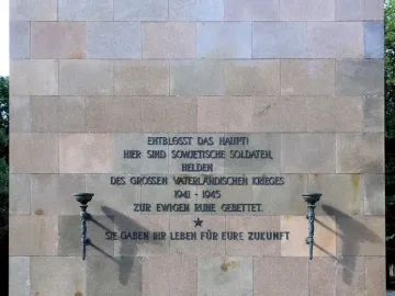 Inscribed stone wall at the Soviet War Memorial Schönholzer Heide, with torch sconces on either side of a star symbol.
