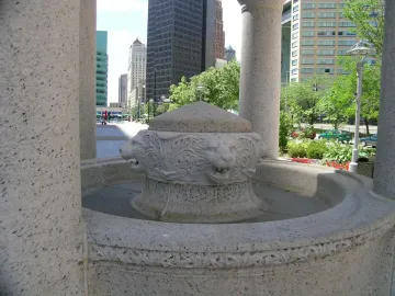 Bagley Memorial Fountain with carved lion heads around the central basin, framed by stone columns and a city skyline in the background.