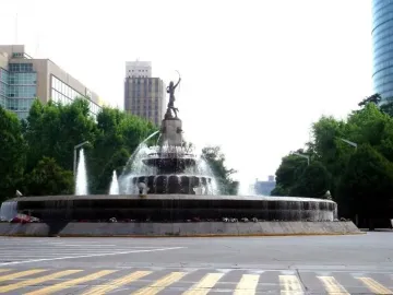 Diana the Huntress Fountain with a tall statue and water spraying from a multi-tiered stone base at a city intersection.