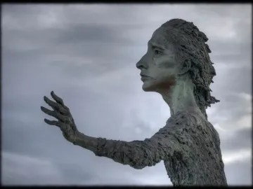 La madre del emigrante bronze statue of a woman standing barefoot with one arm outstretched in a plaza