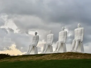 The Man by the Sea sculpture with four white seated figures on a grassy hill under a cloudy sky.