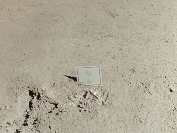 Fallen Astronaut memorial showing a small white astronaut figure lying on a dusty surface beside a partially embedded plaque.