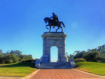 Sam Houston Statue on a stone archway with a rider on horseback above a grassy knoll and brick walkway.