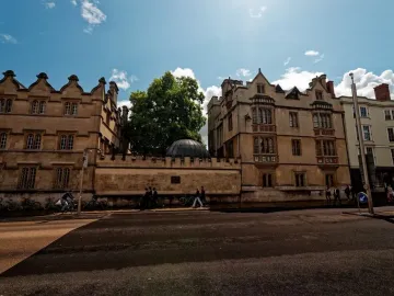 The Shelley Memorial’s dark ribbed dome tops a stone wall between ornate university buildings, with a small plaque below.