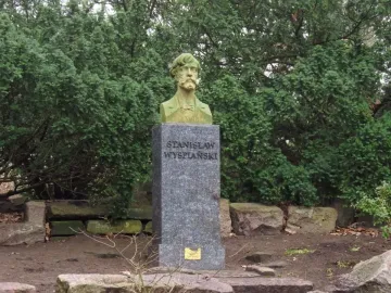 Stanisław Wyspiański bust on a tall stone pedestal in a leafy outdoor setting.
