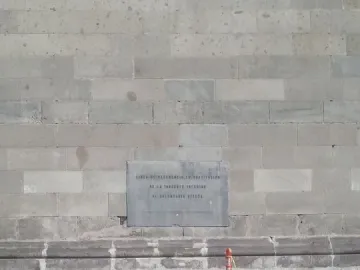 Spanish plaque set into a light stone wall marking the Aztec Sun Stone reference point, with an orange post and metal box nearby.