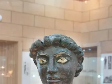 Close-up of the head and upper chest of the Efebo de Selinunte bronze statue with inlaid eyes and curly hair.