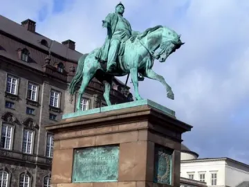 Frederick VII equestrian statue on a tall stone pedestal in a city square.