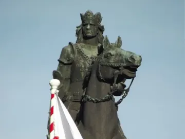 The Grunwald Monument shows a crowned armored rider on horseback against a clear blue sky, with a Polish flag in the foreground.