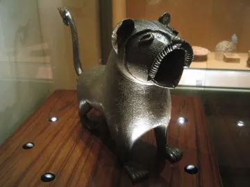 Lion of Monzon sculpture with a curved articulated tail, shown on a wooden surface.