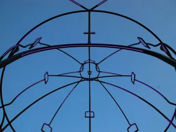 Memoria Urbana’s black metal framework lit with purple lights against a blue sky.