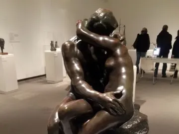 The Kiss bronze sculpture showing two nude figures embracing on a rocky base in a museum gallery.