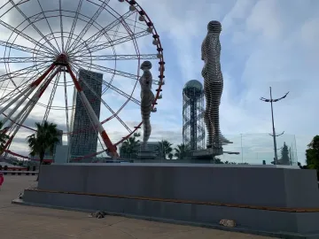 Ali and Nino sculpture with two metallic human figures facing each other on a platform, with a Ferris wheel in the background.