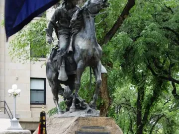 Buckey O\'Neill Monument, an equestrian bronze statue on a rock base, with uniformed people gathered below and a ceremonial flag in front.