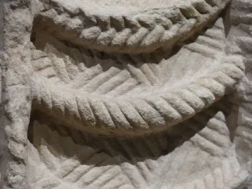 Close-up of light-colored stone relief carving with braided curved bands and woven patterns from the Lady of Cerro de los Santos.