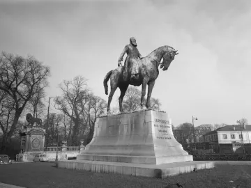 Leopold II equestrian statue on a tall stone pedestal in an open square with bare trees and surrounding buildings.