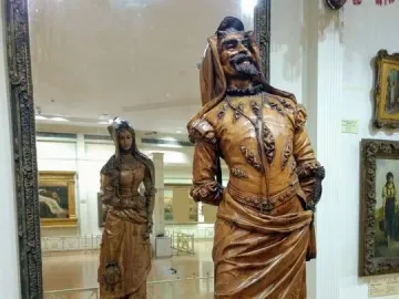Mephistopheles and Margaretta sculpture with a bearded man in elaborate attire and a woman reflected on the reverse side in a mirror.