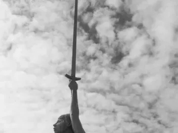 Verity, a bronze sculpture of a pregnant woman holding a sword aloft against a cloudy sky.