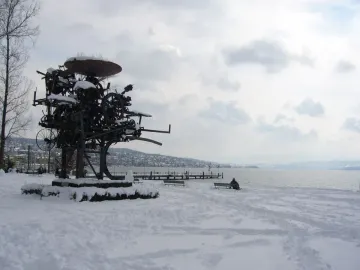 Heureka, a dark metal sculpture of wheels and gears in a snowy lakeside park.
