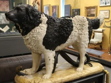 Bashaw sculpture of a dog standing over a coiled snake on a carved cushion.