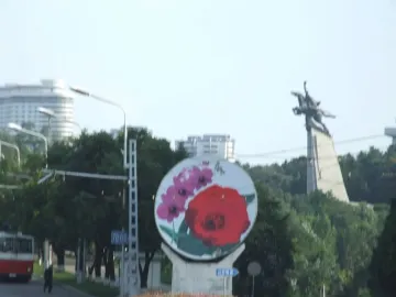 The Chollima Statue appears as a dark silhouette on a tree-covered hill against a bright hazy sky.