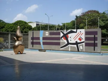Cloud Shepherd, a golden-bronze abstract sculpture, stands beside a colorful geometric wall in a plaza.