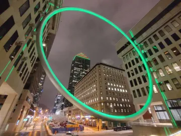 The Ring glows green above a nighttime cityscape with a wet, snowy street below.
