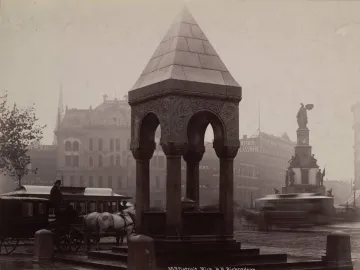 Michigan Soldiers\' and Sailors\' Monument beside an ornate stone canopy, with horse-drawn carriages and city buildings in the background.