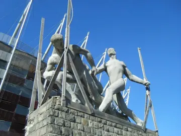 Sztafeta sculpture showing two stone runners in a relay handoff near a stadium.