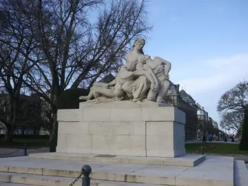 Stone war memorial with a central female figure cradling two other figures on a tiered base with inscriptions.