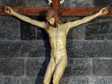 Brunelleschi Crucifix showing a light-colored crucified Christ figure on a dark wooden cross against a stone wall.