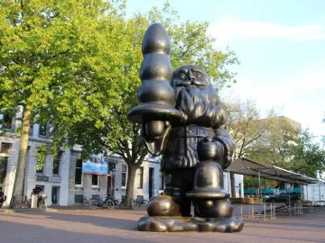 Dark metallic Santa Claus sculpture holding an abstract elongated object in one hand and a smaller object in the other.