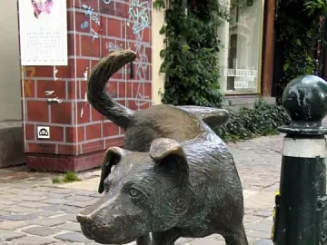 Zinneke Pis bronze dog sculpture on a cobblestone street beside a dark green bollard.