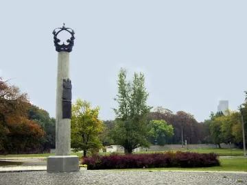 Electio Viritim Monument, a tall pale column topped with a dark crown and relief carvings, standing on a cobblestone base in a park with autumn trees.