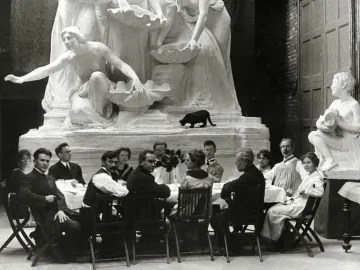 The Fountain of the Great Lakes sculpture stands behind a group of diners seated at a table, with a black cat on the sculpture base.