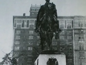 Simón Bolívar equestrian statue on a stone pedestal with men gathered below and a floral wreath at its base.