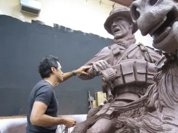 A man stands beside a reddish-brown clay model of America\'s Response Monument, touching the soldier on horseback sculpture.