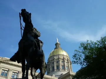 John Brown Gordon statue silhouetted against the Georgia State Capitol dome and blue sky.