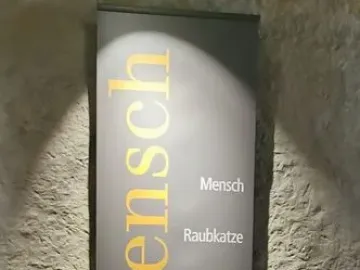 Banner for the Löwenmensch exhibit with golden vertical lettering and a list of related terms on a wall.